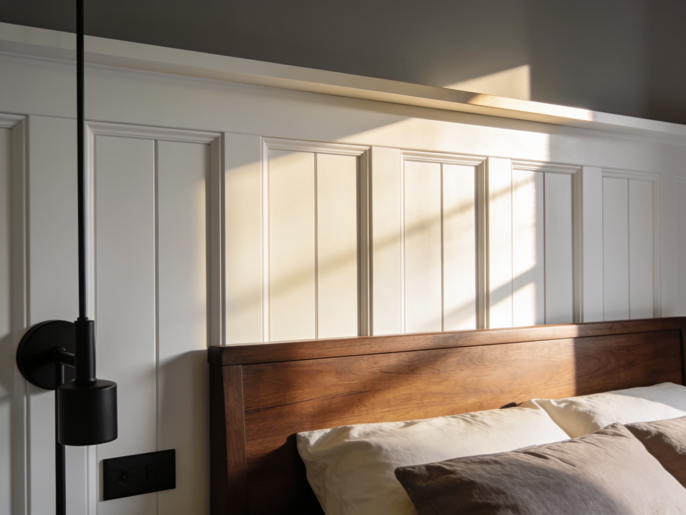 White board-and-batten accent wall behind a farmhouse bed headboard